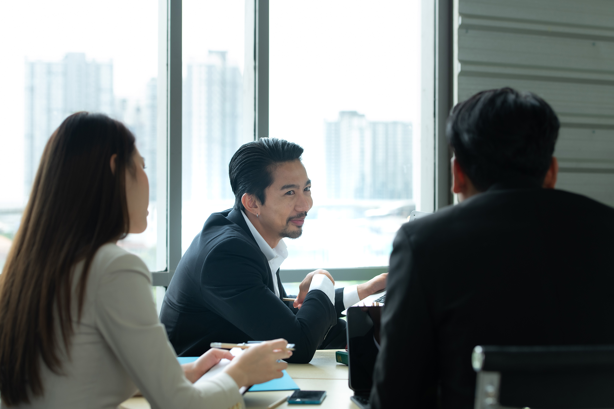 A group of young Asian entrepreneurs. Top Management is meeting to review stock investment data from the team in a meeting room with natural light windows.